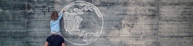 Kind auf den Schultern eines Mannes deutet auf eine gemalte Weltkugel auf einer Mauer