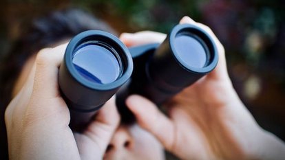 zur Liste mit den Auslagestellen des Programmhefts. Ein Mensch sieht durch ein Fernglas